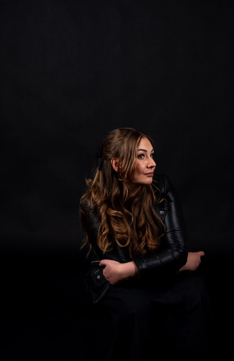 Dark Style – Studio Porträt im AuraMirror Leipzig Frau mit Lederjacke sitzt vor schwarzem Hintergrund im AuraMirror Studio